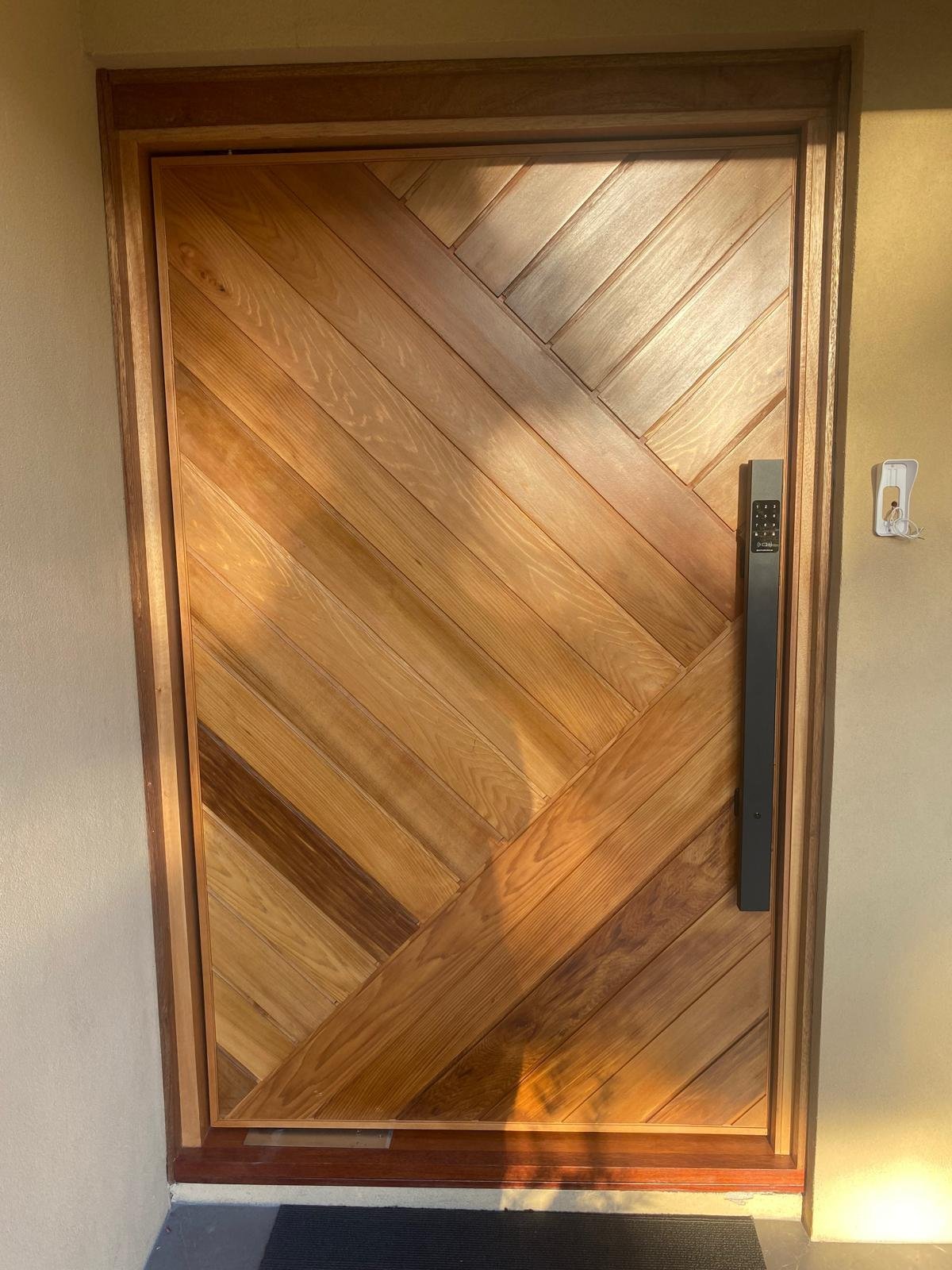 Chevron-patterned timber pivot entry door with a smart lock keypad
