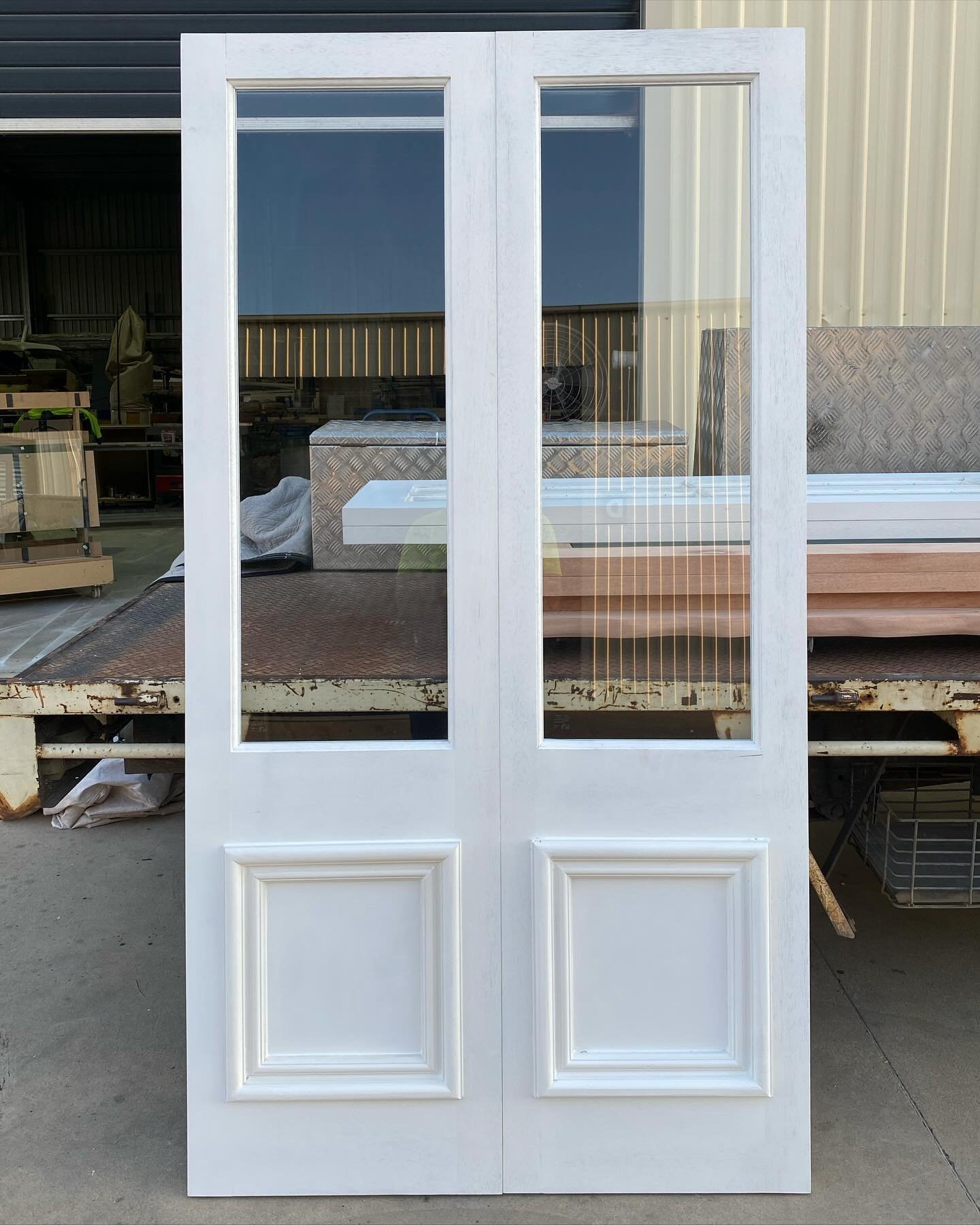 White-painted timber double doors with single-pane glazing over a raised panel, workshop yard