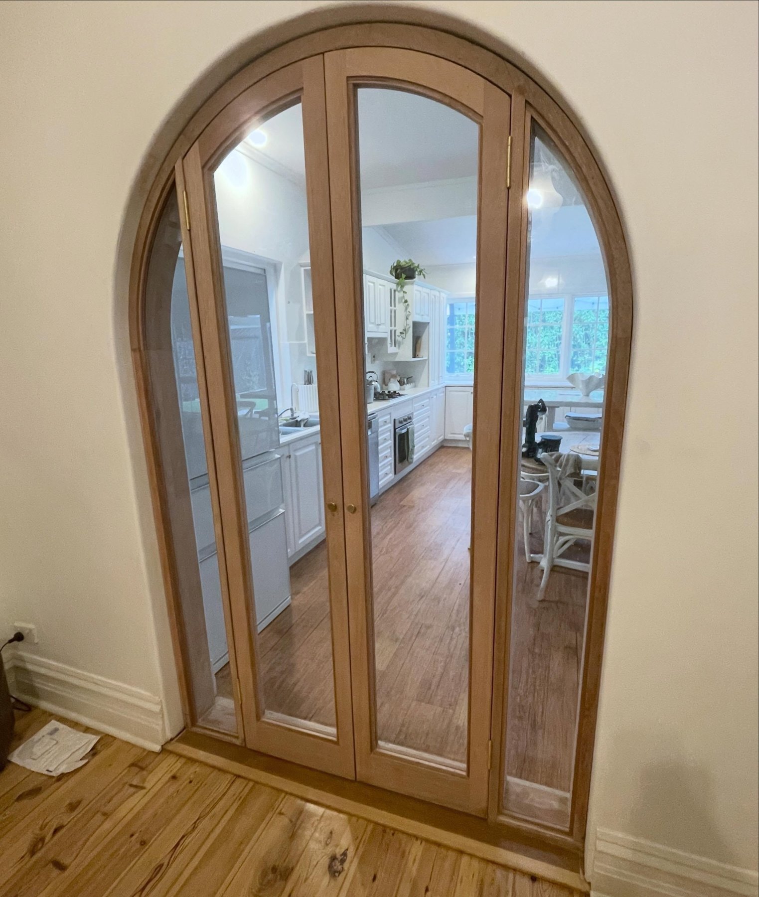 Arched timber bifold doors opening into a kitchen, with glazed panels