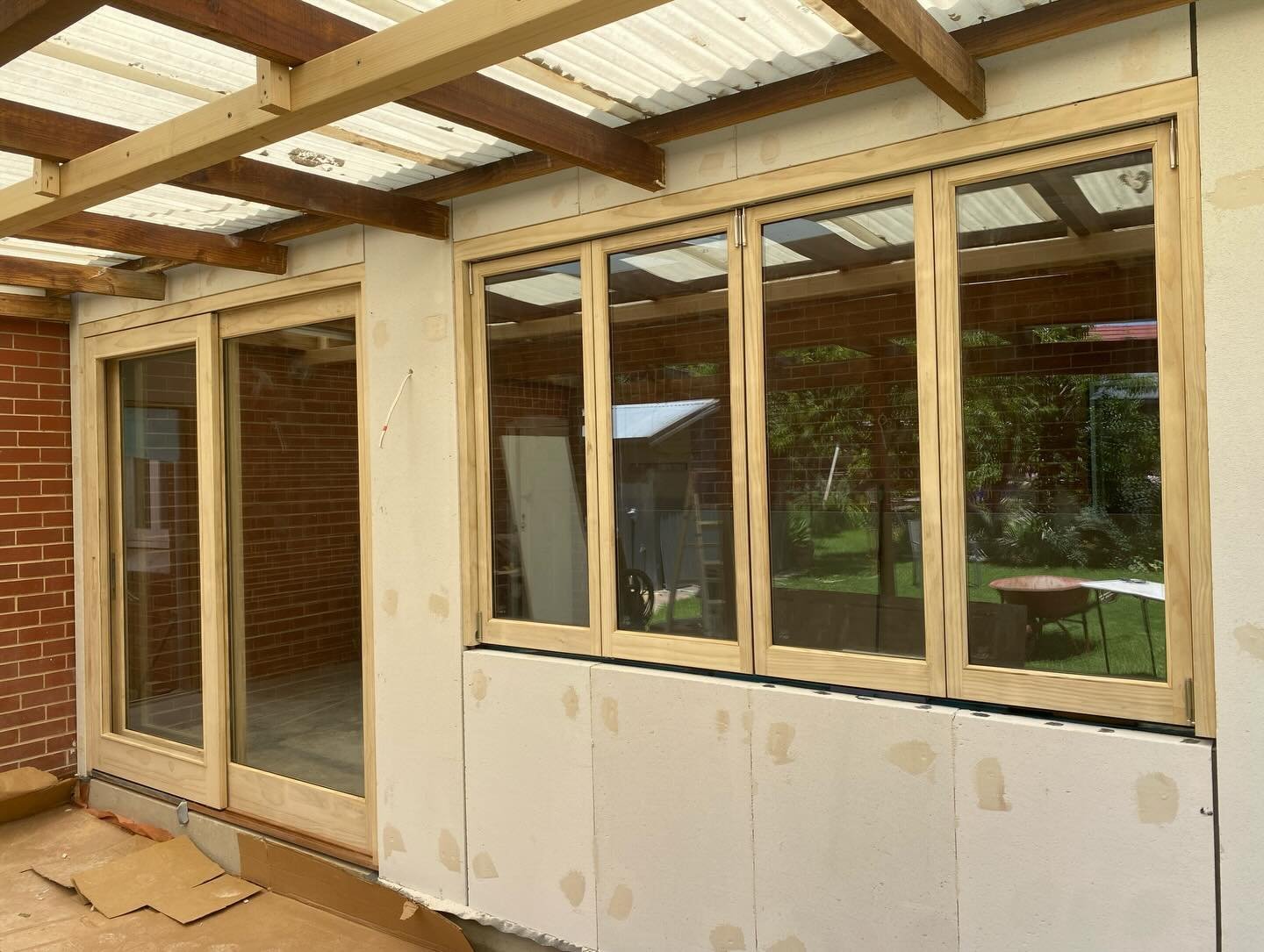 Multi-panel timber casement window bank beside a sliding glass door on a pergola-covered patio