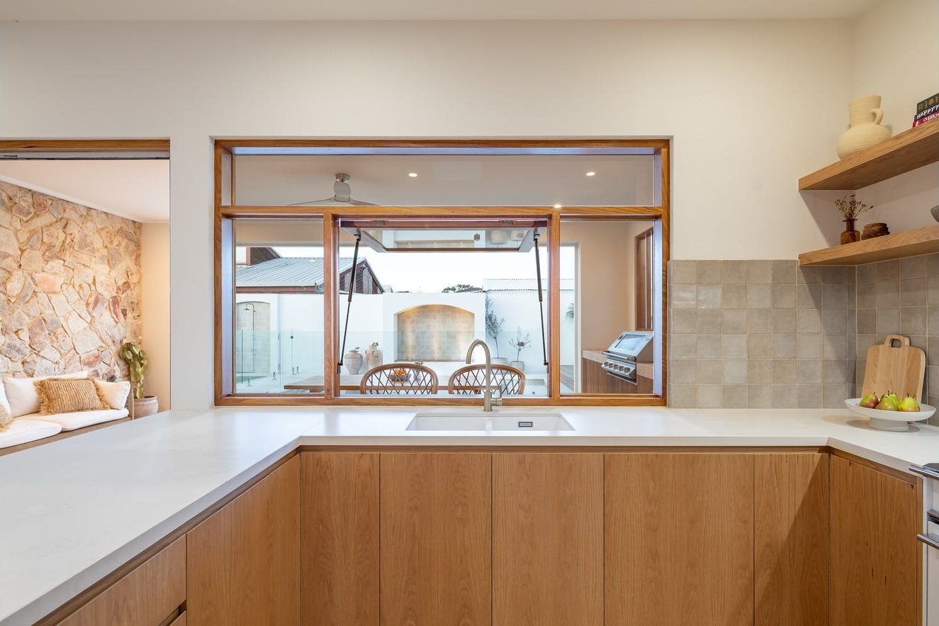 Timber-framed awning servery window opening from the kitchen bench to the outdoor patio