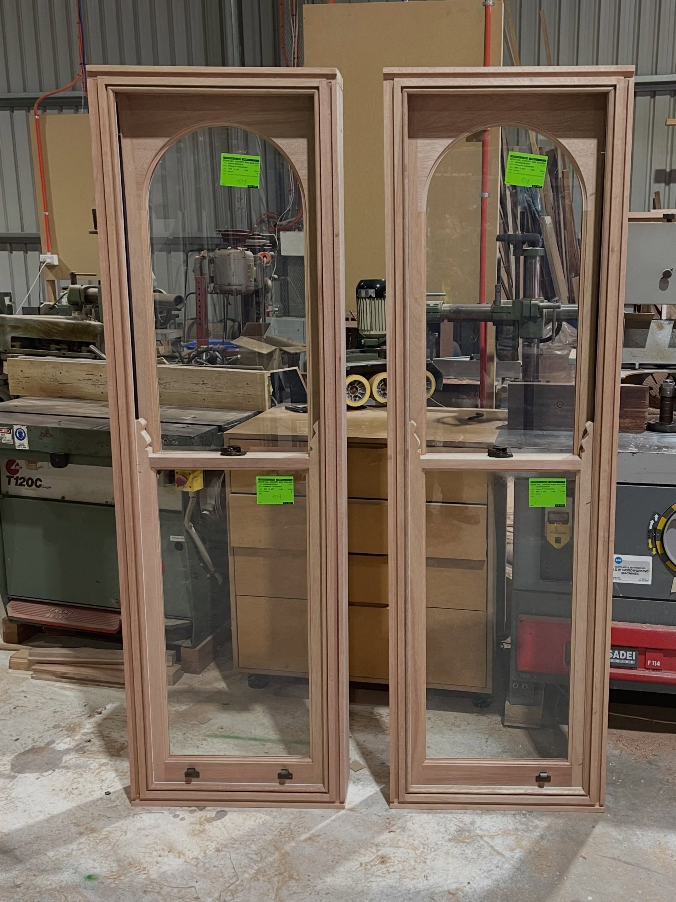 Matching pair of arched-top timber awning windows, workshop with supplier tags