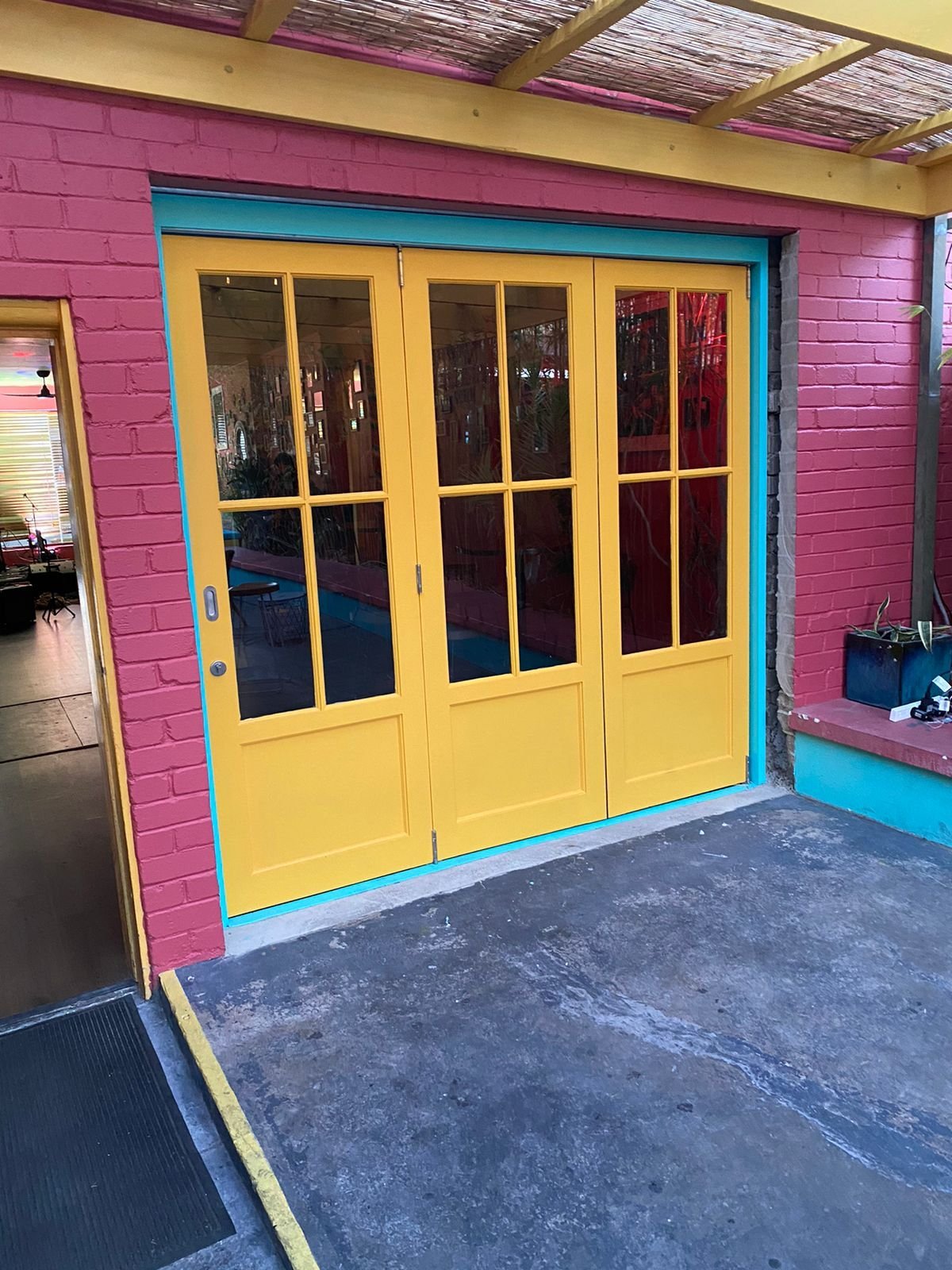 Three-panel yellow-painted timber bifold doors with multi-pane glazing, colorful Miami-style building
